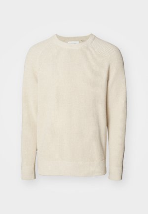 Lys beige genser med ribbestruktur, rund hals, og lange raglanermer. Sidesplitter i kanten for bedre bevegelsesfrihet.