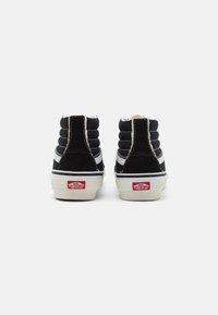 Sorte lerret høye sneakers med hvite detaljer, som har en polstret krage, hvit søm, og en rød logo på hælen.