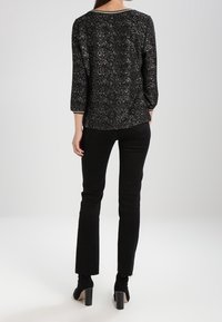 Schwarz-silberner, glitzernder Oberteil mit drei Viertelärmeln, Rundhalsausschnitt und taillierter Passform, kombiniert mit schwarzen Slim-Fit-Hosen und Ankle Boots.