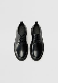 Zapatos de dress de cuero negro con un acabado suave, punta redondeada, diseño de cordones y suela de goma texturizada para mayor agarre. Con detalle de tira de agarre.