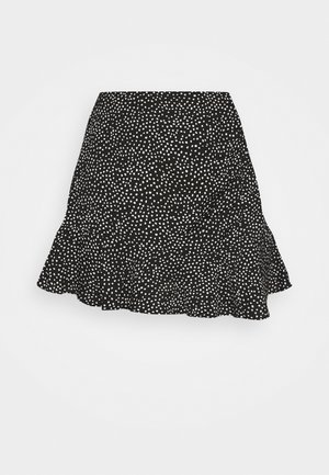 Mini-jupe noire avec motif de points blancs irréguliers et ourlet à volants, présentée sur un fond clair uni.