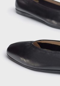 Bailarinas de piel negra con punta redondeada, textura suave y perfil bajo. El interior cuenta con un forro beige y un detalle de costura mínimo.