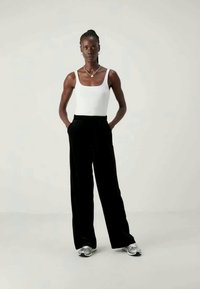 Μαύρο βελούδινο παντελόνι σε φαρδύ ίσιο κόψιμο σε συνδυασμό με ένα στενό λευκό tank top. Το ντύσιμο συνδυάζει μαλακές υφές με μία κομψή σιλουέτα.