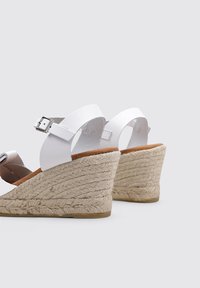 Sandalias de cuña blancas con tacón de yute trenzado, correa ajustable en el tobillo y parte superior de cuero suave en un diseño elegante.