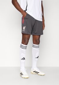 Graue Fußballshorts mit roten Streifen und Liverpool FC-Logo. Kombiniert mit weißen Socken mit schwarzen Akzenten und schwarz-weißen Fußballschuhen.