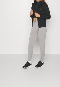 Sweat à capuche noir zippé porté sur un crop top gris, associé à un jogging gris clair et des chaussures de sport noires. Comprend des poches latérales et des cordons de serrage.
