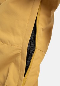 Tessuto giallo con dettagli in zip che rivelano un rivestimento in rete nera. La texture appare liscia e le cuciture sono visibili.