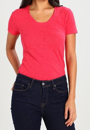 Krótki rękaw t-shirt z żywej różowej tkaniny o gładkiej teksturze i delikatnym melanżowym wzorze, zestawiony z ciemnoniebieskimi dżinsami z subtelnym przeszyciem.