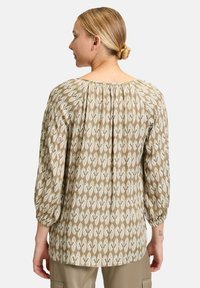 Blusa beige a fantasia con un fit più morbido, scollatura rotonda e dettaglio arricciato sul retro, completata da maniche a tre quarti a sbuffo.