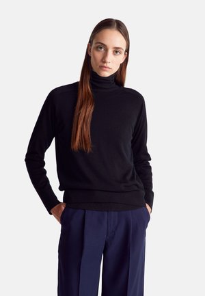 Schwarzer Rollkragenpullover mit langen Ärmeln, nahtlosen Schultern und einem taillierten Saum, kombiniert mit marineblauen, gefalteten Hosen. Glatte Textur.