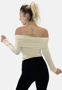 Beige Top mit schulterfreiem Design und langen Ärmeln, Raffung an den Seiten, kombiniert mit schwarzen, hochgeschnittenen Leggings. Glatte Stoffoberfläche.
