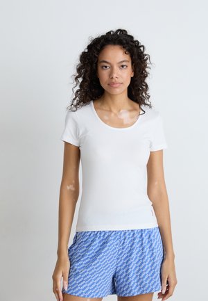 Hvit t-skjorte med korte ermer og rund hals, kombinert med blå mønstrede shorts som har ordet "HUG" i hvitt. Glatt tøystruktur.