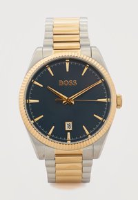 Ρολόι χεριού από χρυσό και ασήμι με μαύρο καντράν, χρυσούς δείκτες ώρας και δείκτες, ένδειξη ημερομηνίας στη θέση 6 και λογότυπο BOSS στη θέση 12.