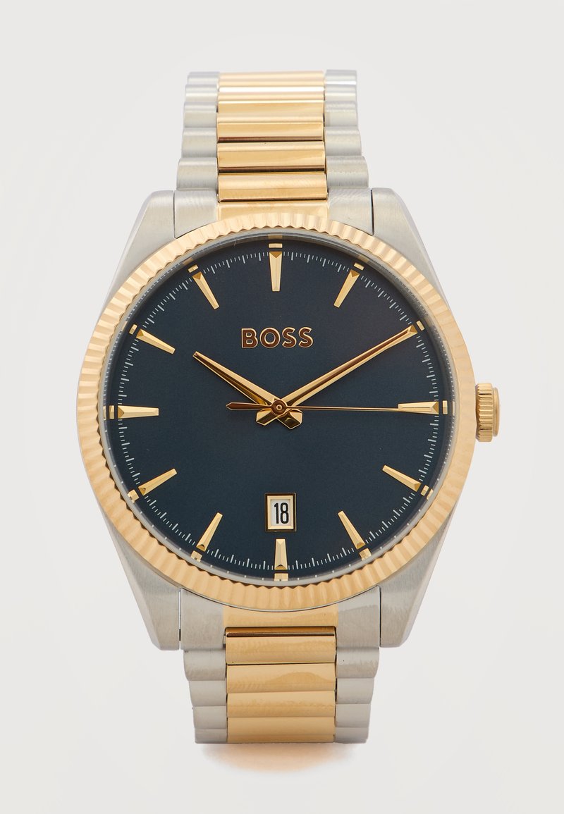 Ρολόι χεριού από χρυσό και ασήμι με μαύρο καντράν, χρυσούς δείκτες ώρας και δείκτες, ένδειξη ημερομηνίας στη θέση 6 και λογότυπο BOSS στη θέση 12.