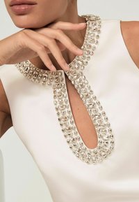 Biele bezramenné šaty s výstrihom v tvare kľúčovej dierky, zdobené čírymi kamienkami pozdĺž goliera. Hladká saténová textúra.