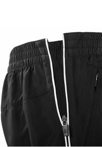 Schwarze Hose mit elastischem Bund, Reißverschlussdetail und kontrastierender weiße Naht. Texturiertes Material mit Taschen an den Seiten.