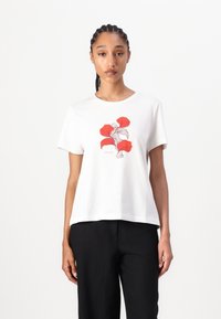 Witte katoenen t-shirt met een rood bloemig grafisch ontwerp op de voorkant. Ronde halslijn en relaxed fit. Gepaard met zwarte broeken.
