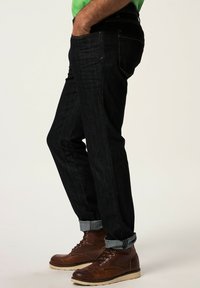 Mörkblå denimjeans med rak passform, uppvikt fåll och gula sömnadsdetaljer, kombinerade med bruna läderstövlar.