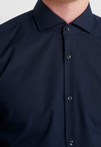 Navyblauw overhemd met een spreidkraag, voorzien van een gladde textuur en zes zwarte knopen aan de voorkant, goed gestructureerd en netjes op maat gemaakt.