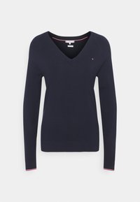 Svetr s výstřihem do V a dlouhými rukávy v námořnické modři, vyrobený z pletené látky. Obsahuje červené a bílé akcenty na výstřihu a manžetách. Malé logo na hrudi.