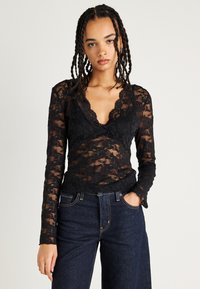 Zwarte kant lange mouwen top met een diepe V-hals en bloemmotieven. Gecombineerd met donkere denim jeans, met een ontspannen pasvorm.