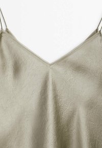 Camisole en satin beige clair avec fines bretelles spaghetti et tissu subtilement texturé sur fond blanc.