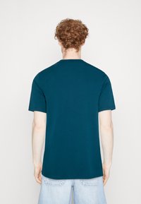 Camiseta de algodón color azul verdoso con mangas cortas y cuello redondo. La parte trasera muestra una textura suave sin adornos ni patrones.