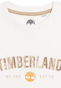 Witte katoen T-shirt met een ronde halslijn, met "TIMBERLAND" in bruine en beige blokkentekst en een boomlogo in oranje.
