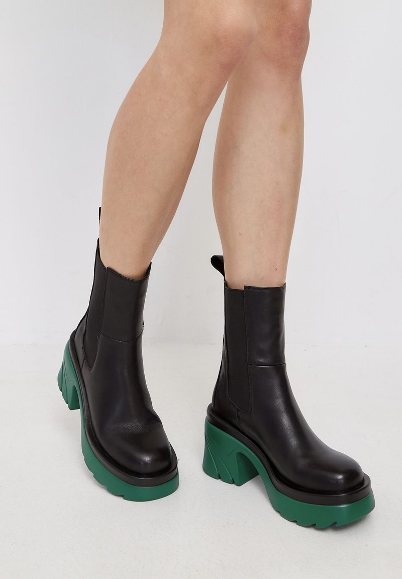 Botas de tobillo de cuero negro con un tacón grueso verde, con una textura suave y paneles laterales elásticos para un fácil calzado.