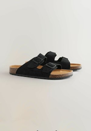 Sandales noires tressées avec deux sangles ajustables et boucles. Semelle intérieure en liège et semelle extérieure en caoutchouc texturé pour une bonne adhérence. Design plat.