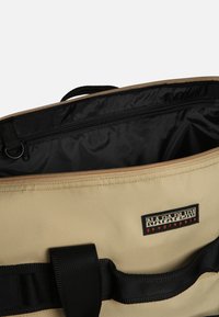 Borsa in tela beige con foderatura interna nera e tasca con zip. Presenta una tracolla nera e una etichetta con logo nera e arancione.
