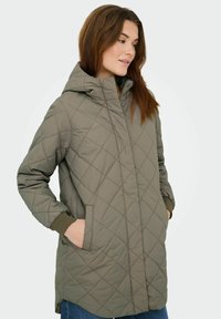 Prešita jakna z kapuco v olivno zeleni barvi z diagonanim šivom. Ima sprednje žepe in rebraste manšete. Lahka, priložnostna zasnova.