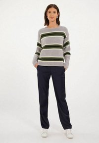 Pull rayé gris avec des bandes vertes et blanches, associé à un pantalon foncé et des baskets blanches. Le pull a une coupe décontractée et un col rond.