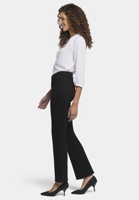 Vaqueros negros de pierna recta de mezclilla, combinados con una blusa blanca y tacones de punta negra, mostrados en un perfil lateral.