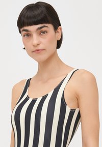 Black and cream striped swimsuit with a scoop neckline and wide shoulder straps. Smooth, stretch fabric with contrasting stitching details.