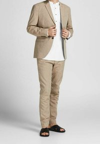 Beige linneset med kavaj med slag och slim-fit byxor, kombinerat med en vit skjorta med knappar och svarta sandaler.