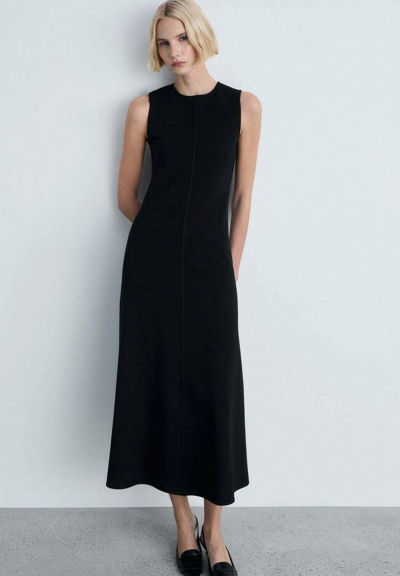 Schwarzes ärmelloses Midikleid mit geradem Schnitt, das mit einer Vordernaht und glatter Textur versehen ist, kombiniert mit schwarzen Slippers.