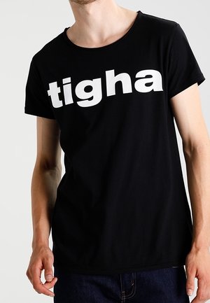 Schwarzes T-Shirt mit kurzen Ärmeln und rundem Ausschnitt, das einen auffälligen weißen Schriftzug "tigha" auf der Brust zeigt. Das Material ist weich und hat eine glatte Textur.
