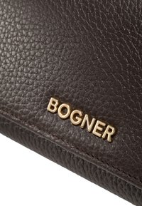 Borsa a tracolla in pelle marrone con superficie texturizzata, con logo dorato "BOGNER". Il bordo presenta un dettaglio di cucitura ordinato.