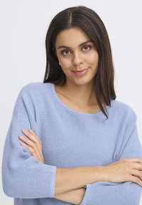 Gais blue krāsas adīts džemperis ar apaļu kakla izgriezumu un trim ceturtdaļām piedurknēm. Strukturēts audums ar brīvu piegriezumu.