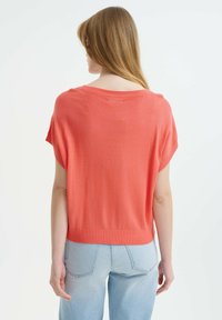 Top corto corallo a maniche corte con un ampio scollo, texture a maglia e una vestibilità ampia, abbinato a jeans a vita alta azzurri.
