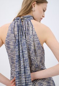 Robe dos nu en tissu à motifs avec des points bleus et beiges. Texture douce avec un dos drapé et un détail de bouton au cou.