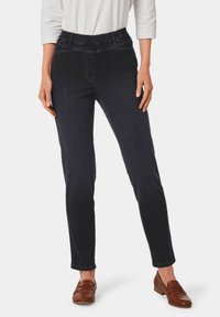 Dunkelblaue Jeans mit elastischem Bund und schmaler Passform. Glatte Textur, knöchellang, ergänzt durch braune Slipper.