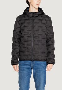 Giubbotto piumino nero con texture a righe orizzontali, chiusura a zip e cappuccio. Indossato con jeans blu, dotati di polsini e orlo elasticizzati.
