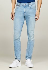 Hellblaue Skinny-Jeans aus Denim, mit klassischem Fünf-Taschen-Design und subtilen Verwaschungen, kombiniert mit weißen Sneakers.