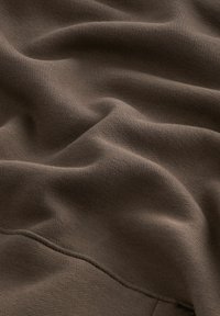 Tissu marron doux avec une texture fine de maille visible et des plis subtils créant des ombres et des reflets délicats.