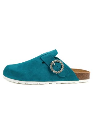 Sabots en suède teal à enfiler avec un bout rond, une sangle ajustable et un accent circulaire en strass ; semelle en liège et semelle en caoutchouc blanche.