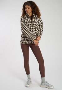 Pullover in pile marrone e crema con motivo houndstooth, con mezza zip, abbinato a leggings marroni e calzini alla caviglia grigio chiaro.