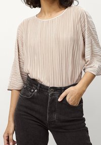 Blusa plissettata rosa chiaro con maniche ampie abbinata a jeans neri a vita alta con chiusura a bottone e tasche laterali.