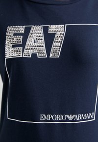 Tumed puuvillane T-särk, millel on hõbedane rhinestone "EA7" logo valge äärisega ja allosas tekst "EMPORIO ARMANI".